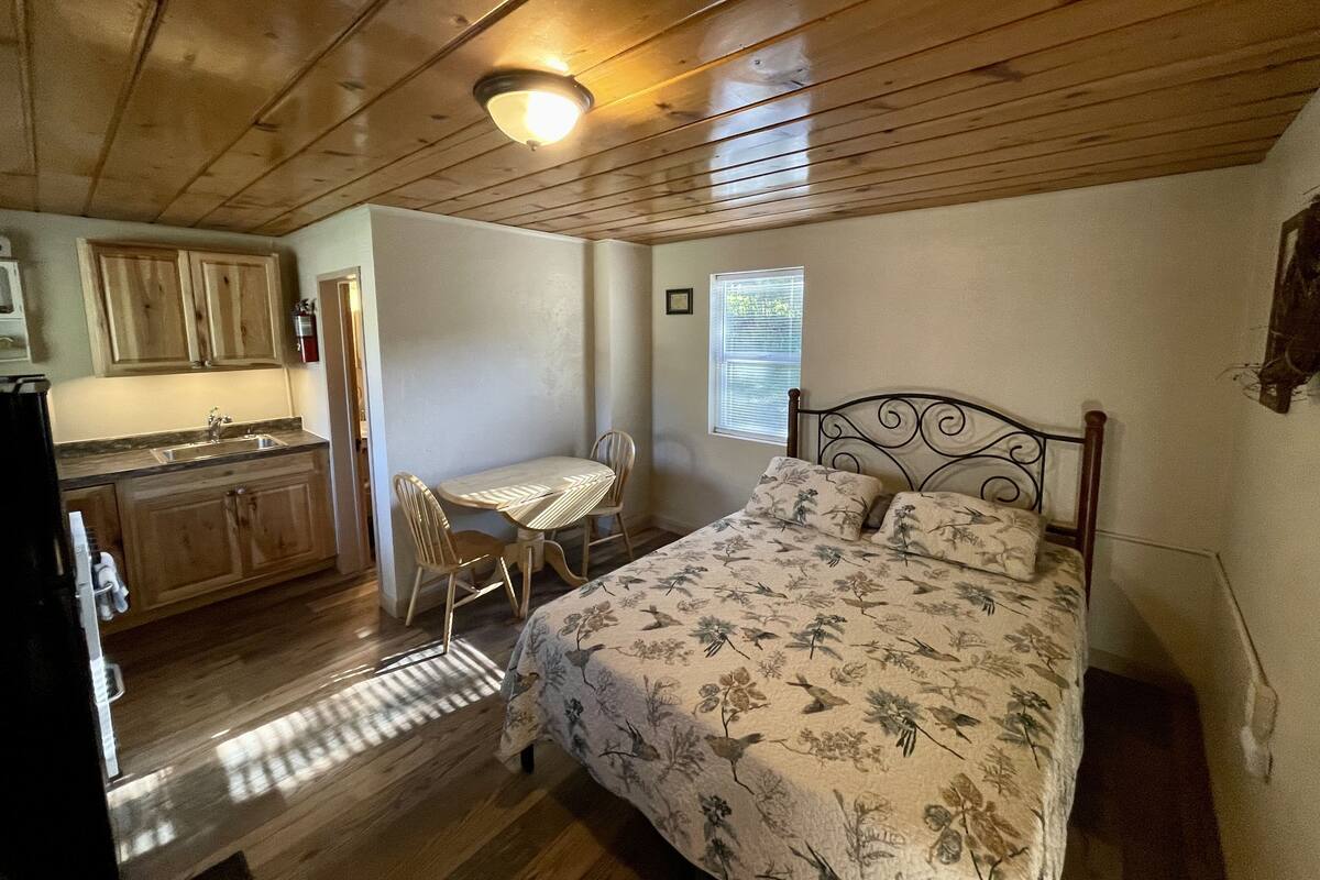 Una habitación pequeña con cama, una mesita y una kitchenette.