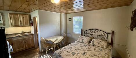A compact room with a bed, a small table, and a kitchenette.