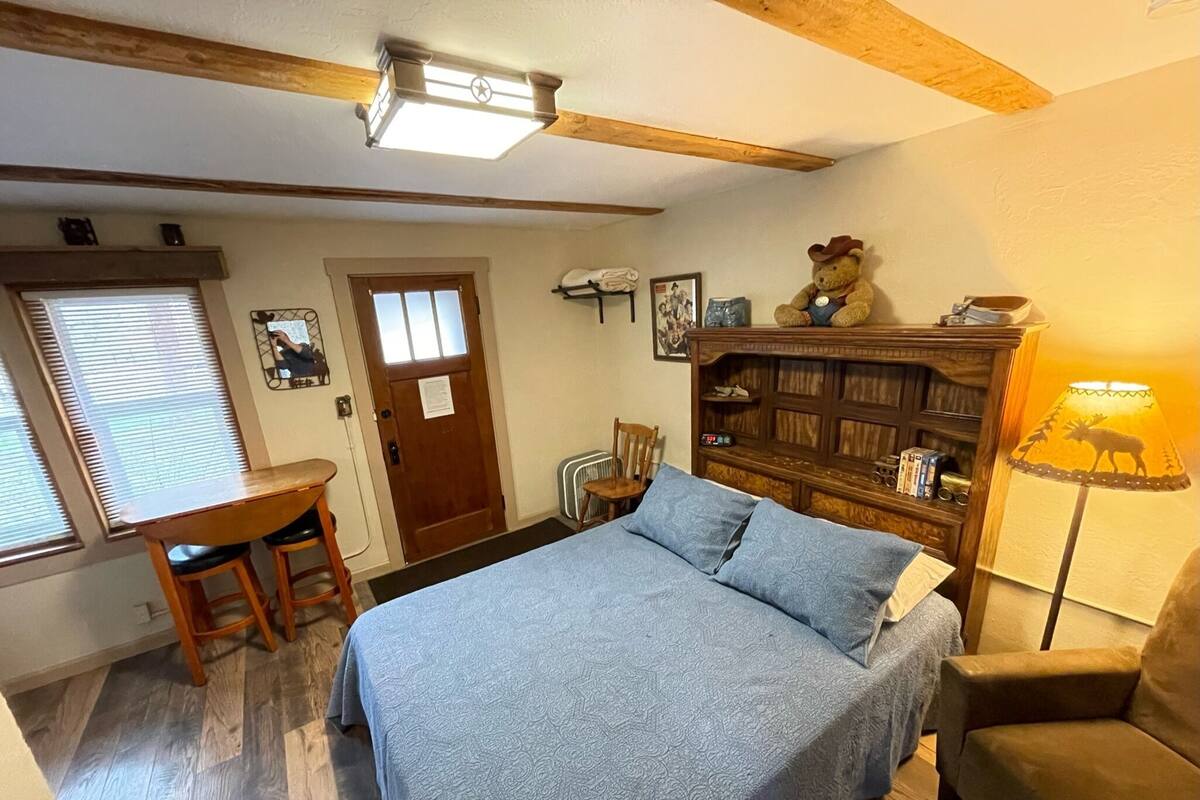 Un dormitorio con cama, escritorio, silla, estantería y lámpara.