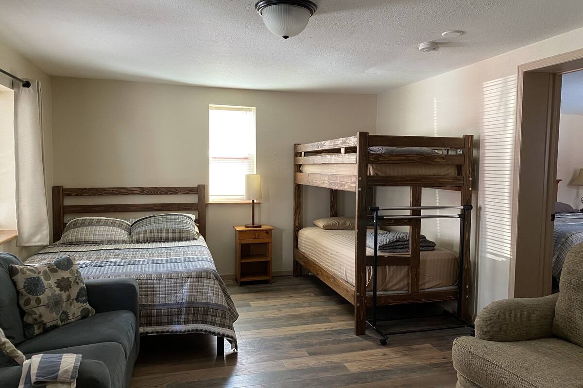 Una habitación con una cama individual, un sofá, una mesita de noche con lámpara y una ventana que deja entrar luz natural.