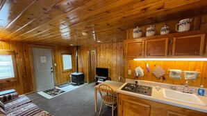 A cozy cabin interior with a wooden interior, a fireplace, a dining area, and a kitchen with wooden cabinets and a stove. - Stoney River Lodge (Loveland)