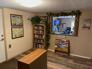 A cabin-themed reception area with a wooden desk, a bookshelf, and a sign indicating it's an office. - Stoney River Lodge (Loveland)