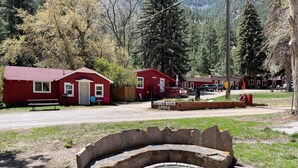 A rustic lodge with red cabins, a stone fire pit, and a sign indicating 'Stoney River Lodge'. - Stoney River Lodge (Loveland)