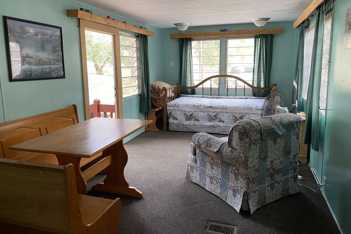 Una habitación con una cama, una mesa y una silla. Hay una ventana con cortinas y un cuadro en la pared.