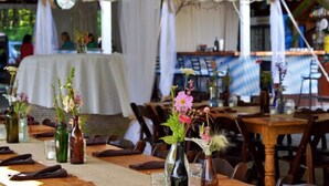 Un área de comedor cubierta con carpas, mesas dispuestas para invitados, jarrones con flores y un ambiente de estar relajado.
