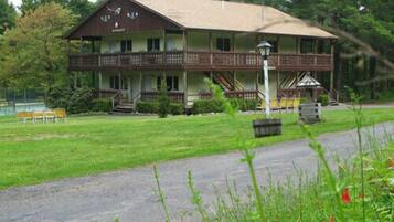 A two-story building with a porch, a staircase, and a lawn with chairs.