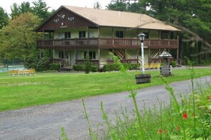A two-story building with a porch, a staircase, and a lawn with chairs.