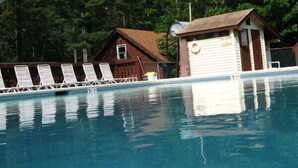 Una piscina con sillones de descanso, una torre de salvavidas y un pequeño edificio con techo.