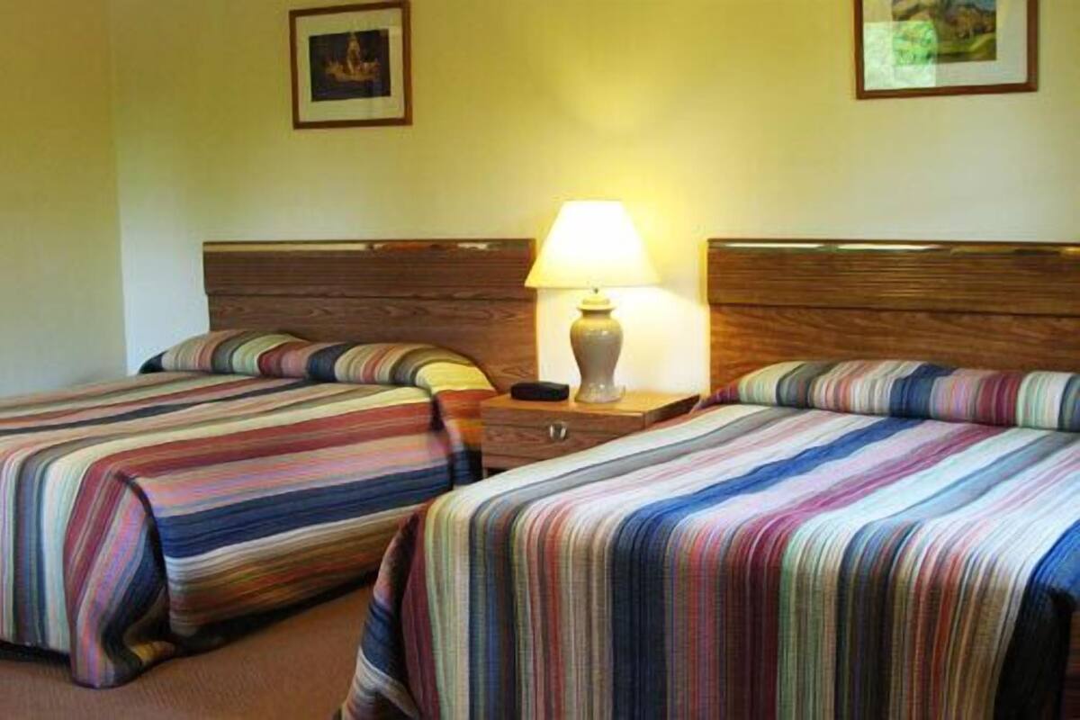 A hotel room with two beds, each with striped bedding, a nightstand with a lamp, and framed pictures on the wall.