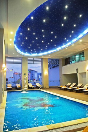 Una piscina interior con techo estrellado, sillones de descanso y vistas a la ciudad.