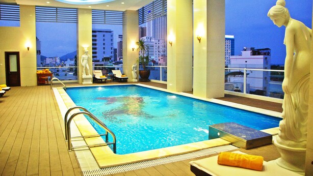 An indoor swimming pool with a view of the cityscape, a statue, and a sun lounger. - Green World Nha Trang Apartment (Nha Trang)