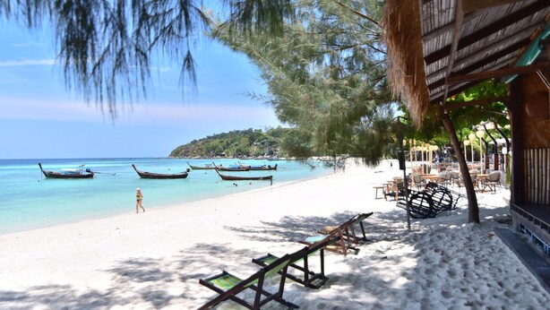 A beach with thatched-roof structures, lounge chairs, and boats in the water. - Green View Beach Resort (Koh Lipe)