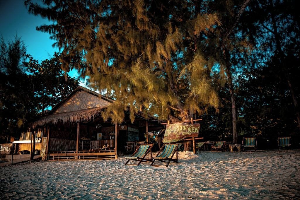 A beachside resort with a thatched-roof building, lounge chairs, and a sign indicating a view of the sea.