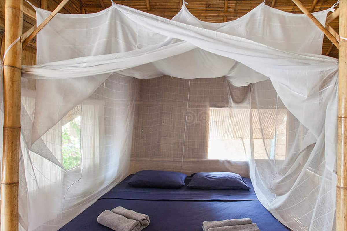 A room with a bed under a white canopy, bamboo walls, and a window.