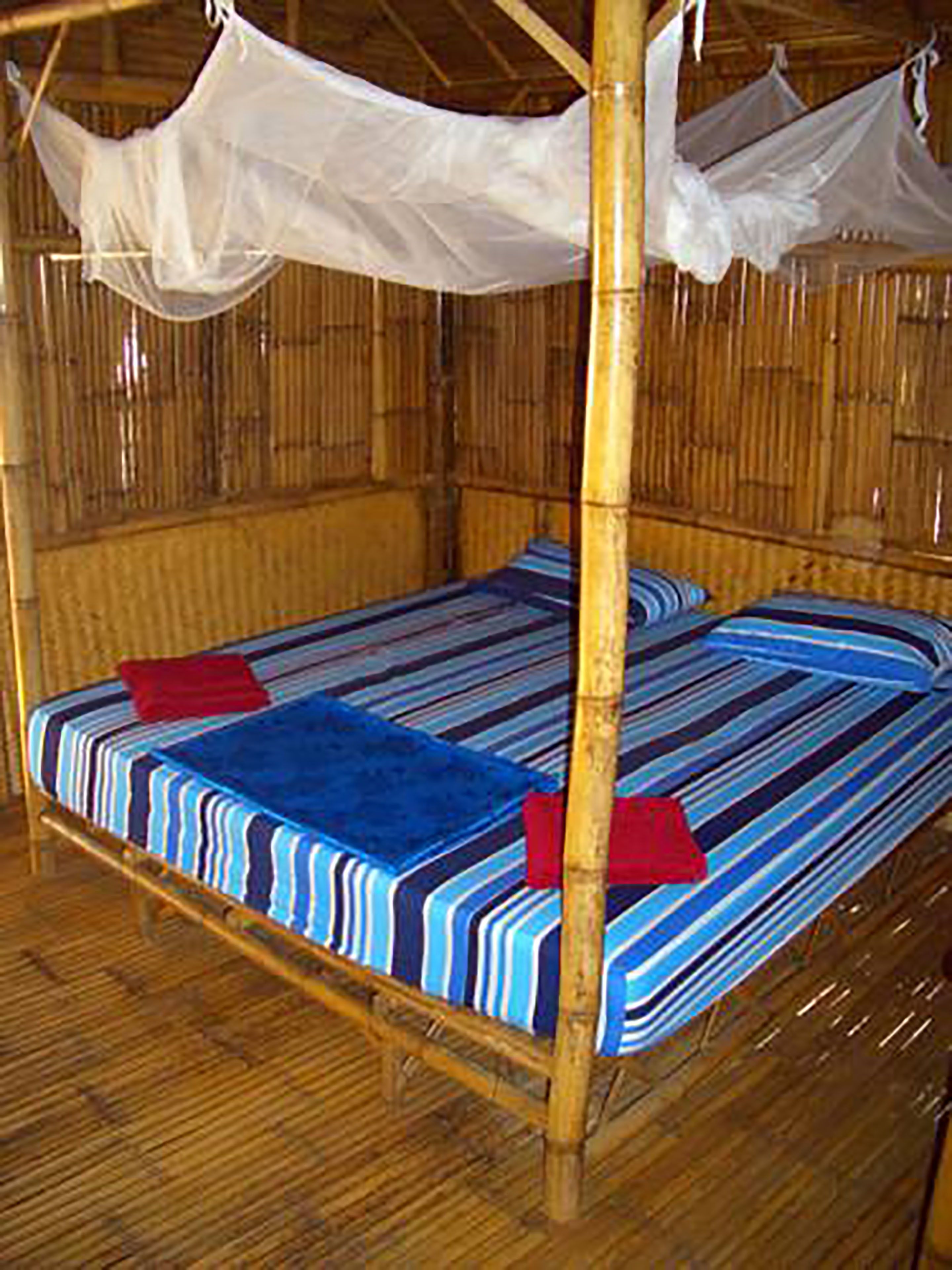 Una cama individual con una colcha a rayas, dos almohadas, un dosel y una pared de bambú.