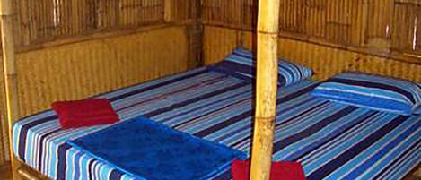 Una cama individual con una colcha a rayas, dos almohadas, un dosel y una pared de bambú.