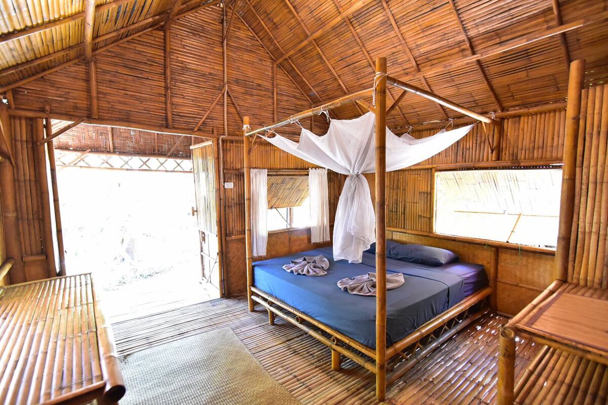 A room with a four-poster bed, a window with curtains, and a wooden floor.