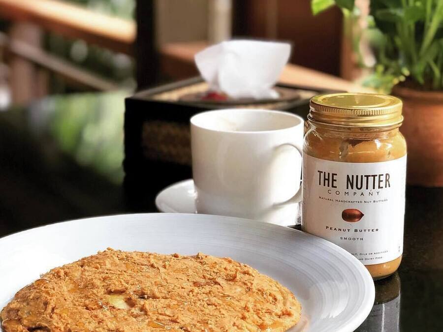 A plate of cookies, a jar of peanut butter, and a white cup on a table with a plant in the background.