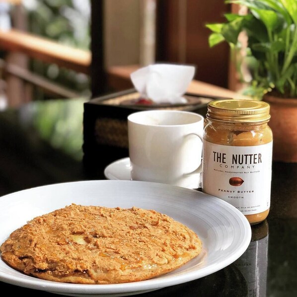 Une assiette de biscuits, un pot de beurre de cacahuète et une tasse blanche sur une table, avec une plante en arrière-plan.