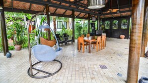 A covered outdoor seating area with a swing chair, a dining table with chairs, and potted plants. - Cocoville Phuket Resort (Chalong)