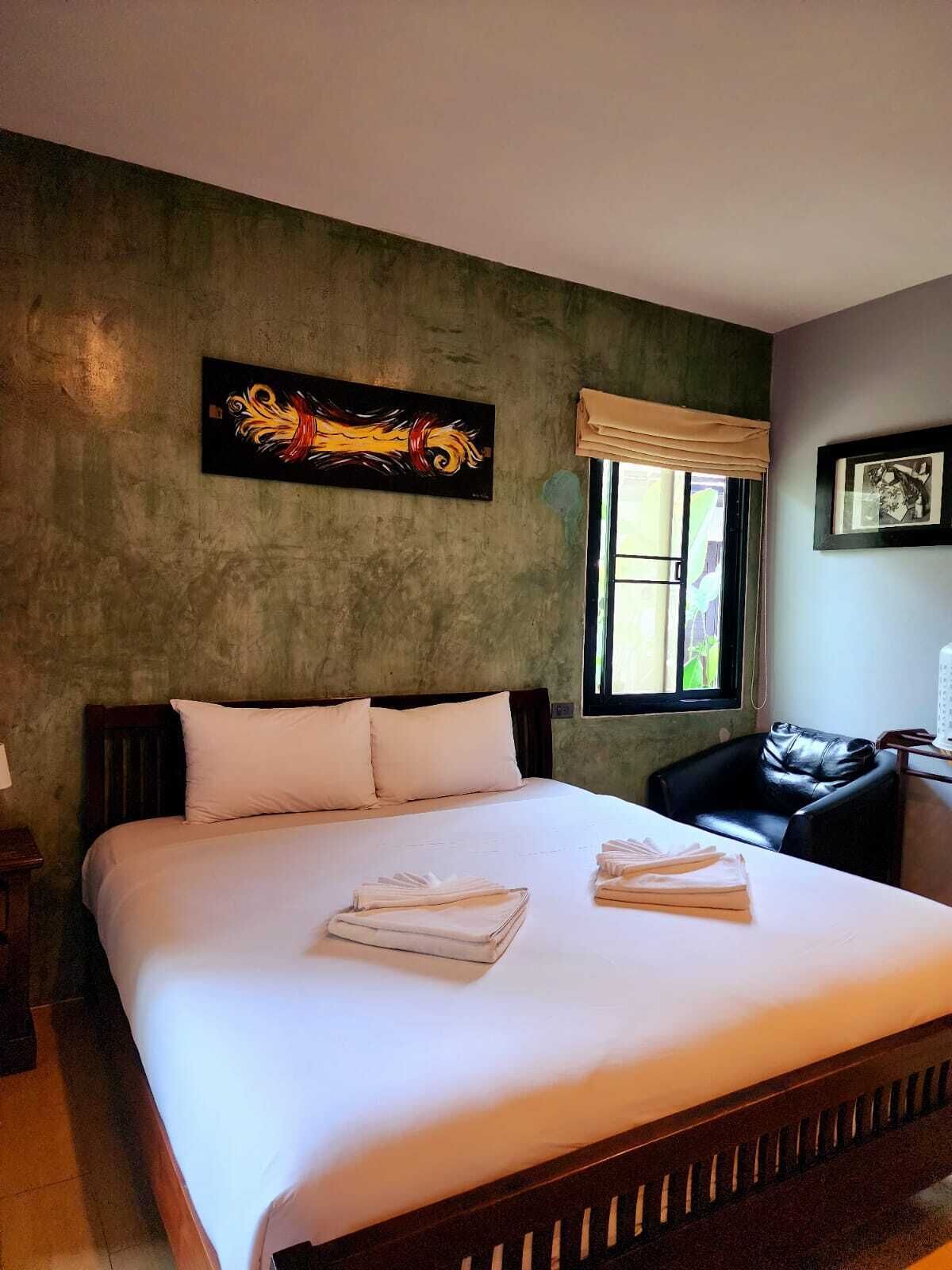A hotel room with a large bed, a window with a view, a painting on the wall, and a chair.