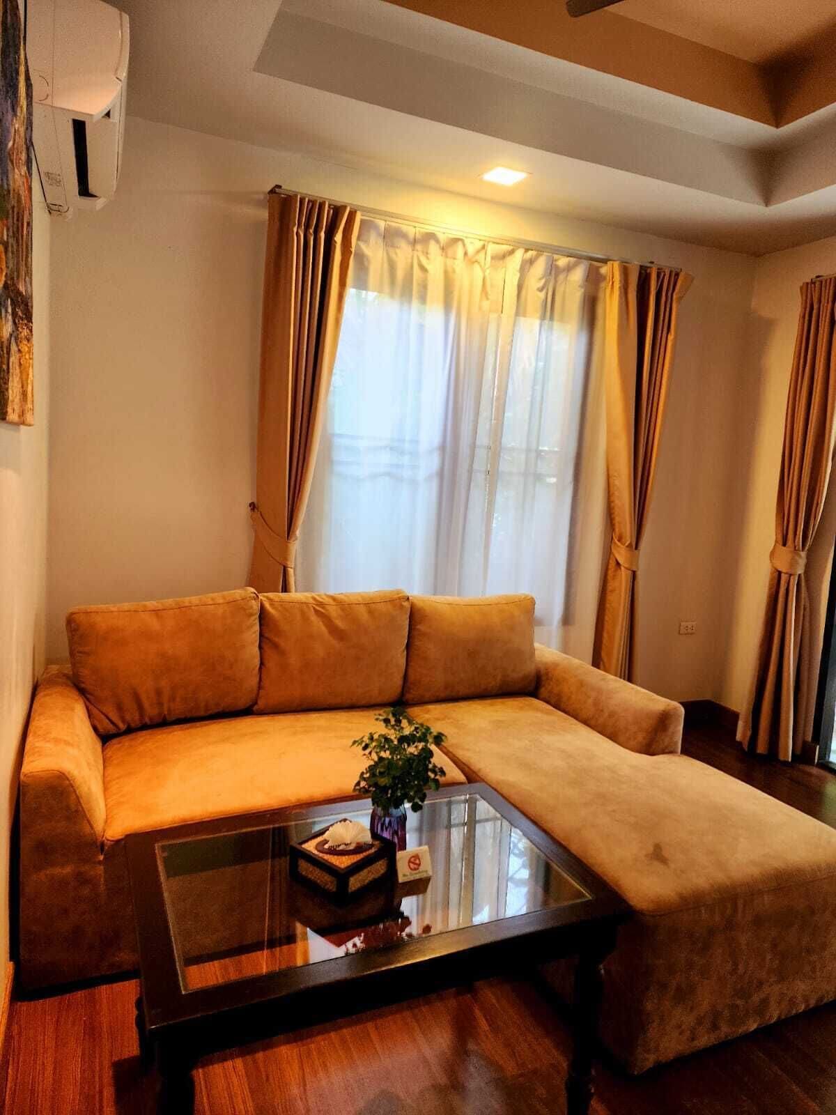 A living room with a sofa, a glass coffee table, and a potted plant.
