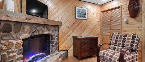 A cozy room with a stone fireplace, a television mounted above it, and a patterned armchair.