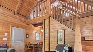 A wooden cabin interior with a dining area, a sofa, a staircase, and a ceiling with wooden beams. - Wild Pacific Waterfront Cabins (Ucluelet)