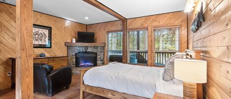 Un dormitorio de cabaña de madera acogedor, con chimenea de piedra, cama, escritorio y televisor.