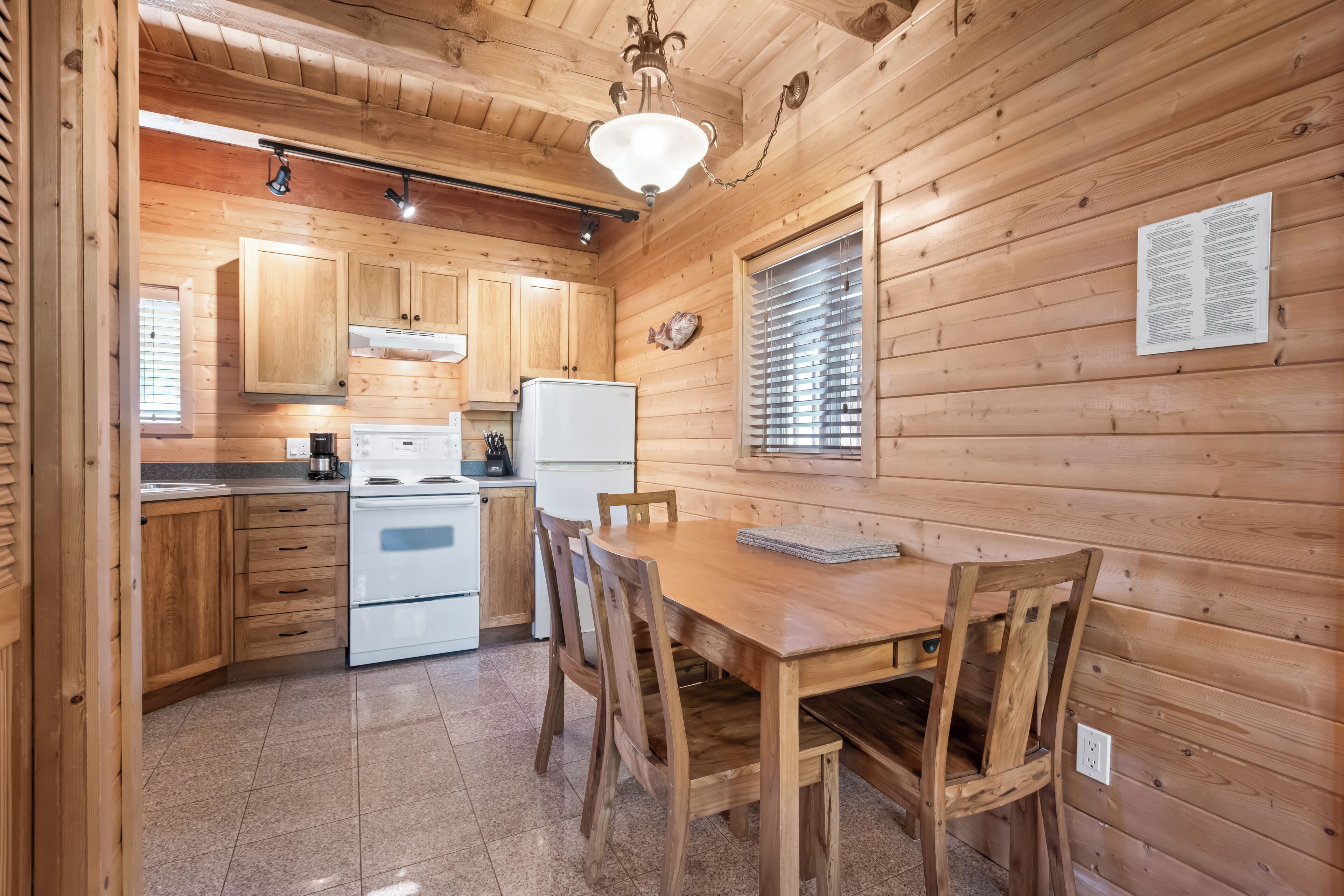 A wooden cabin kitchen with a dining table and chairs, a refrigerator, stove, and cabinets.