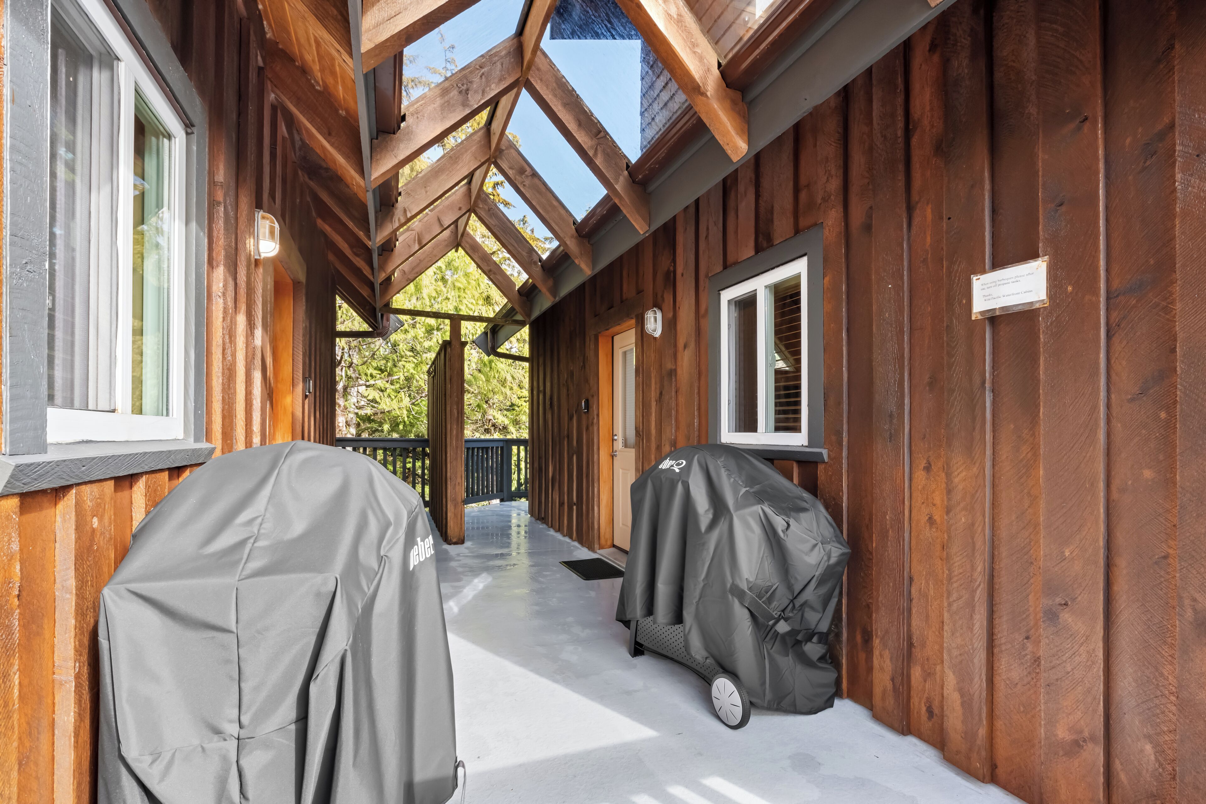 A covered outdoor area with wooden walls and a skylight, featuring barbecue grills and a covered grill cart.