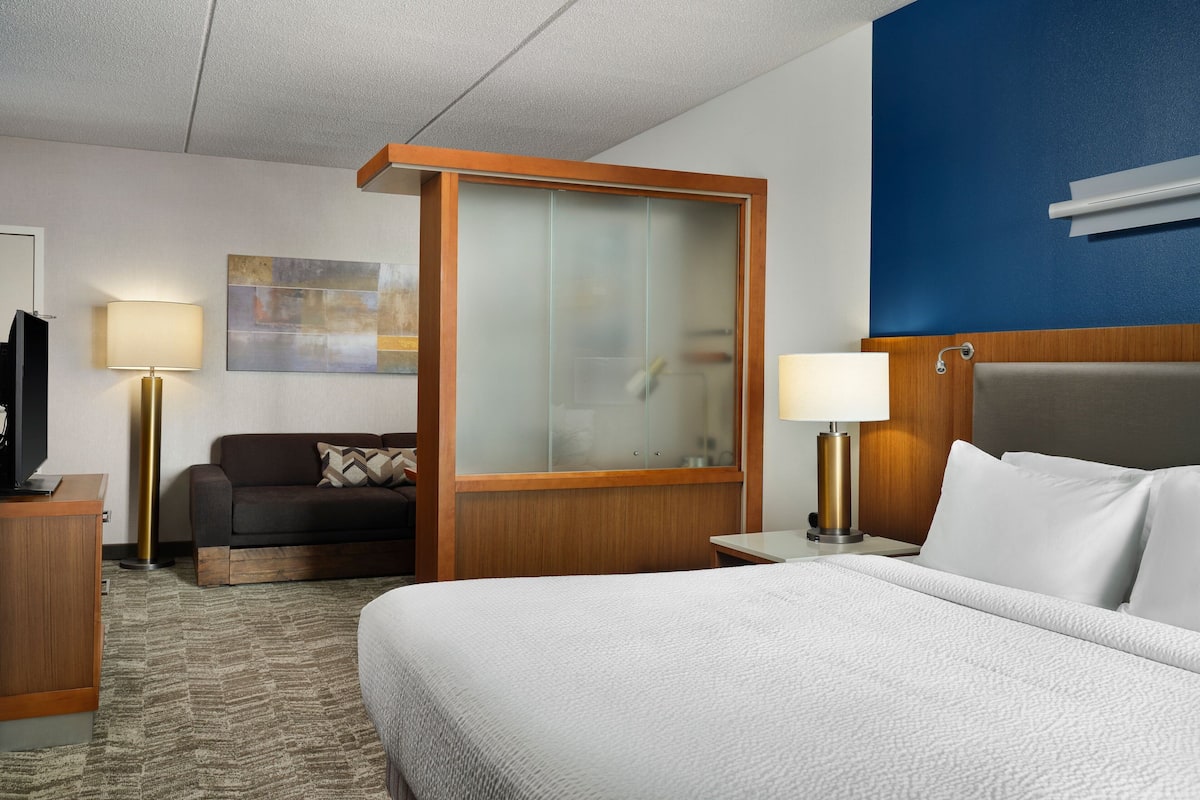 Ein Hotelzimmer mit Bett, Schreibtisch, Sofa und einer Glastrennwand.
