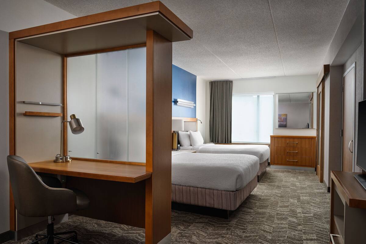 Ein Hotelzimmer mit Schreibtisch, zwei Betten, Fernseher und Kleiderschrank.