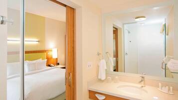 A hotel room with a bed, bedside lamp, and a large mirror above a sink.