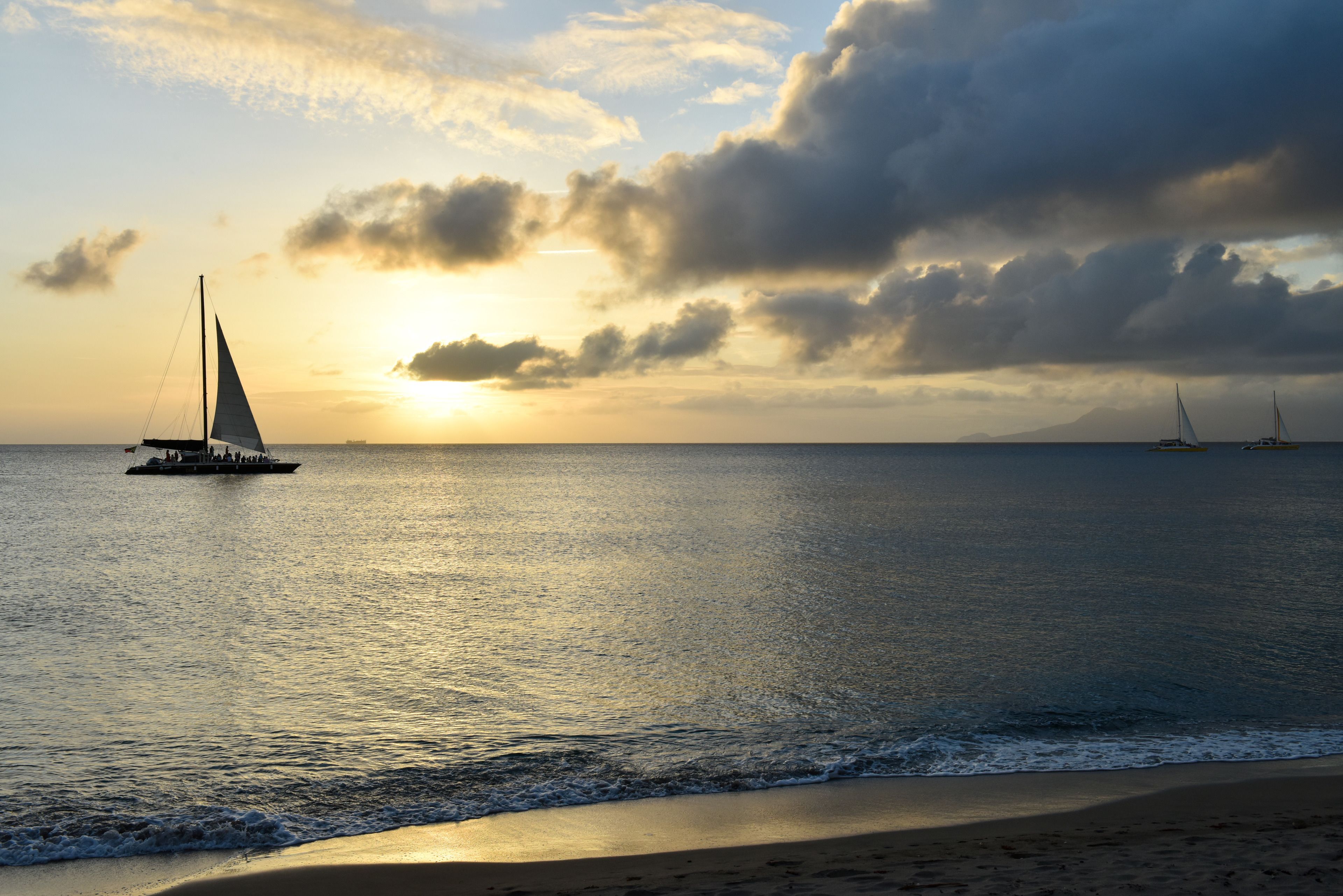 A beach scene with a sailboat and another boat in the distance, under a cloudy sky.