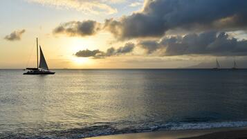 A beach scene with a sailboat and another boat in the distance, under a cloudy sky.