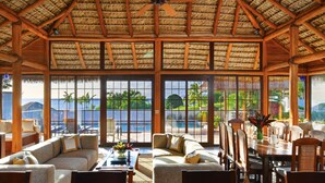 A spacious room with a thatched roof, large windows, and a view of the pool and palm trees. - Paradise Beach Nevis (Cotton Ground)