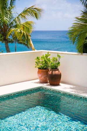 A pool with clear blue water, surrounded by a white balcony with two terracotta pots.