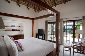 A bedroom with a large bed, wooden headboard, a TV on a small table, a balcony with a view, and a chair. - Paradise Beach Nevis (Cotton Ground)