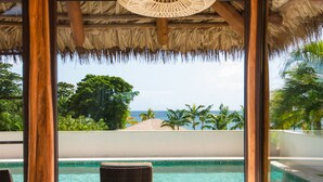A room with a large bed, a hanging wicker chandelier, and a view of the ocean. - Paradise Beach Nevis (Cotton Ground)