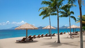 A beach with thatched umbrellas, wooden lounge chairs, and palm trees. - Paradise Beach Nevis (Cotton Ground)