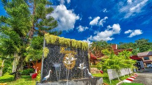 A building entrance with a stone wall, a logo, and decorative bird sculptures. - Sai Rougn Residence (Patong)