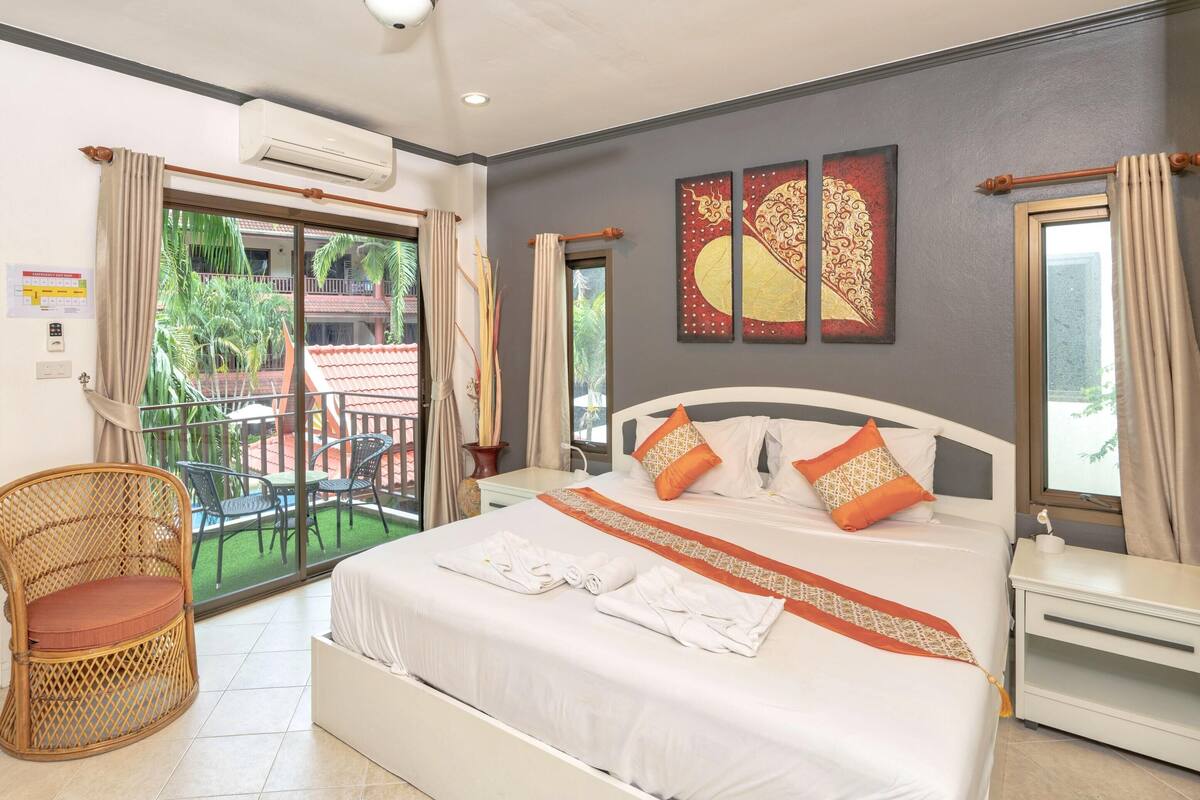 A hotel room with a bed, a chair, a balcony, and a view of palm trees.