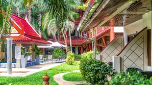 A hotel courtyard with a red-roofed building, palm trees, and a pathway. - Sai Rougn Residence (Patong)