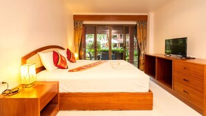A hotel room with a bed, wooden nightstand, TV, and a view of the outdoors. - Sai Rougn Residence (Patong)