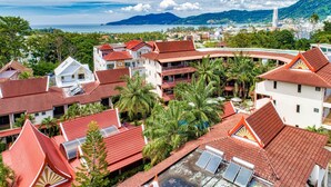 A coastal resort with red-tiled roofs, palm trees, and a view of the sea and mountains. - Sai Rougn Residence (Patong)
