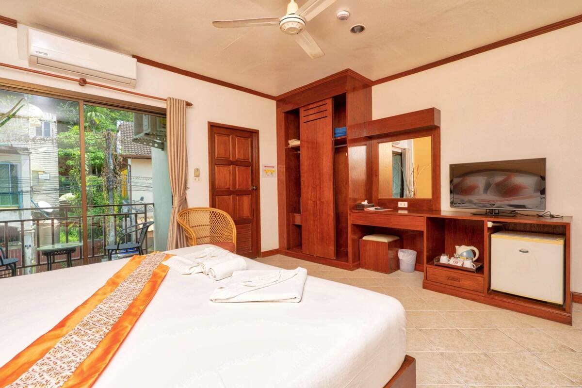 A hotel room with a large bed, a desk with a television, a wardrobe, and a balcony with a view of the outside.