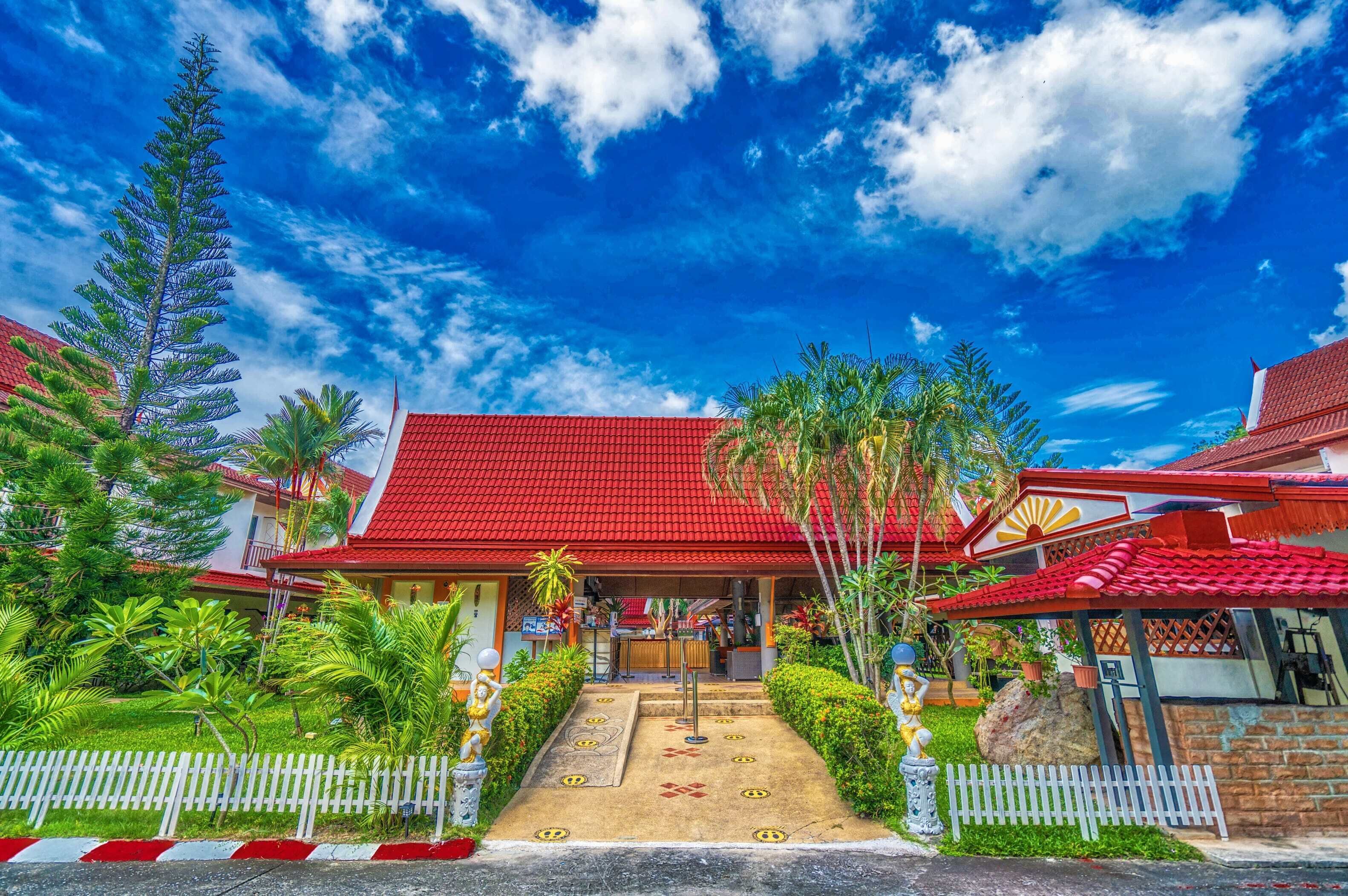 A traditional building with a red roof, surrounded by lush greenery and a white picket fence.