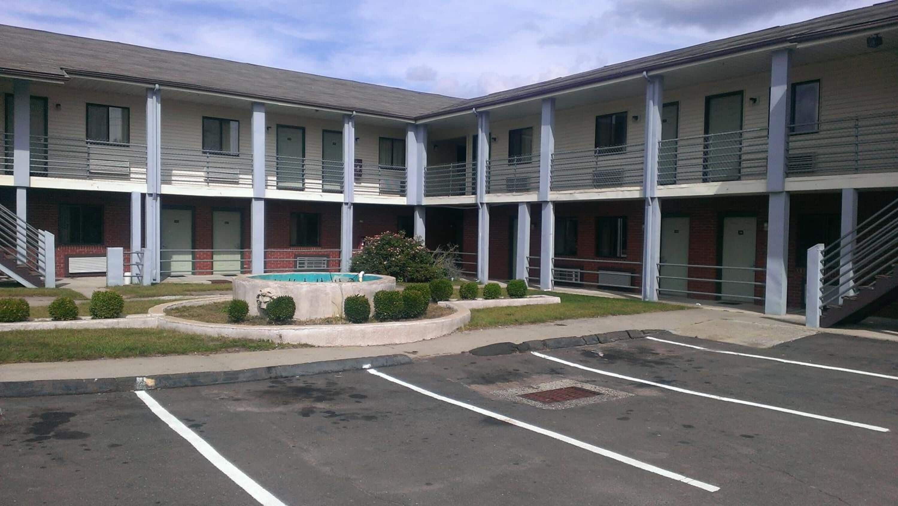 A multi-story motel with a central courtyard, outdoor pool, and parking lot.