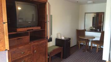 Une chambre d’hôtel comprenant un meuble de rangement en bois, une télévision, une petite table avec une chaise, un miroir et un lit.